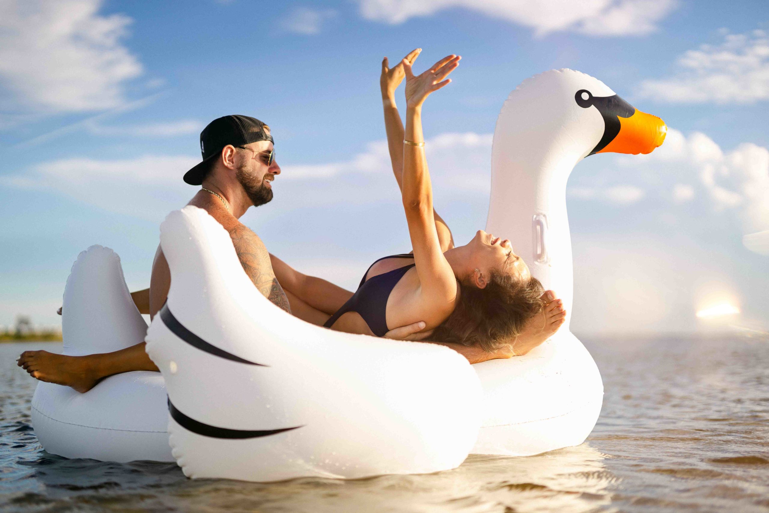 Cute couple have fun floating around in the bay on a swan floaty!